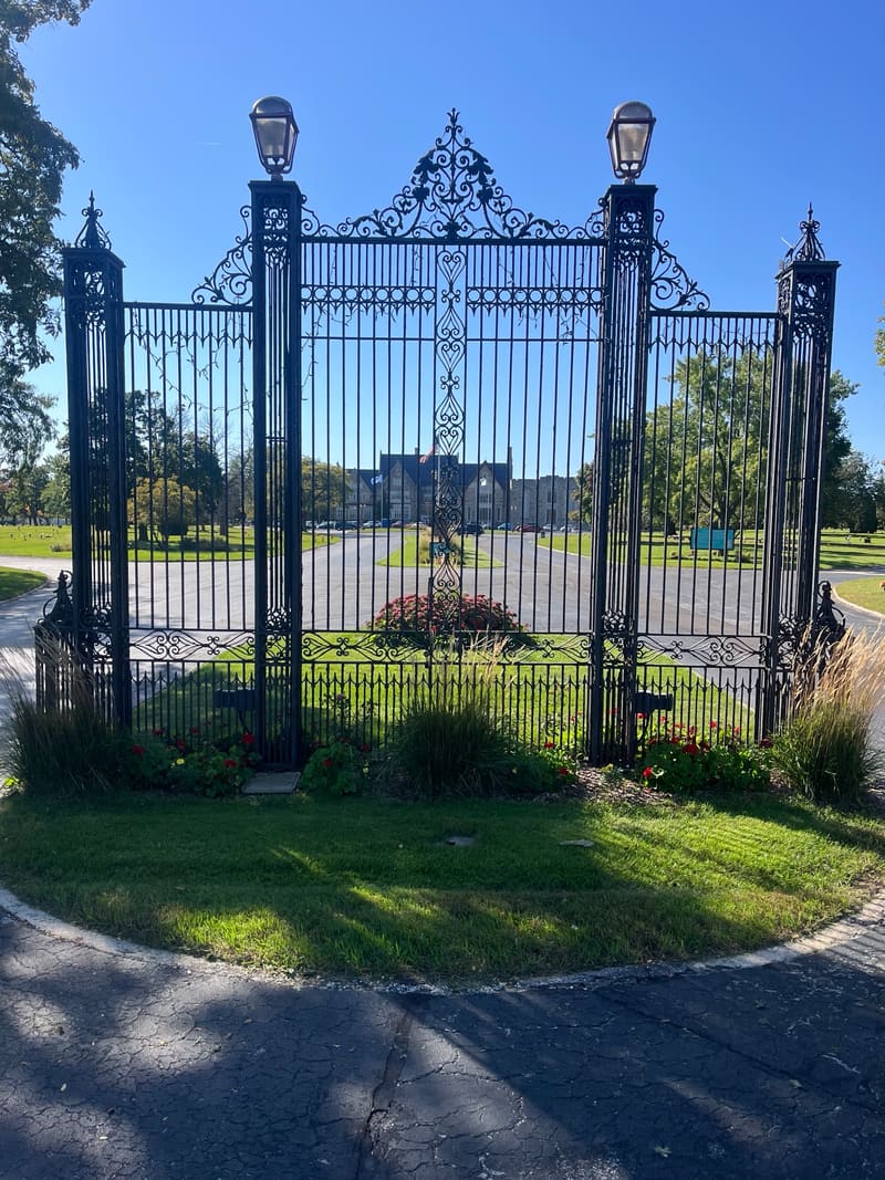 Ornate wrought-iron gates with lamp posts, opening onto a drive.